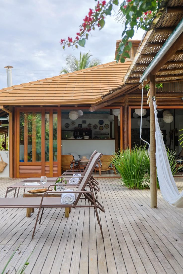 Deck de madeira com espreguiçadeiras, toalhas enroladas, mesa e rede entre as plantas